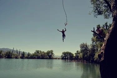 Stock photo of a person swinging on a rope and launching into a large lake.